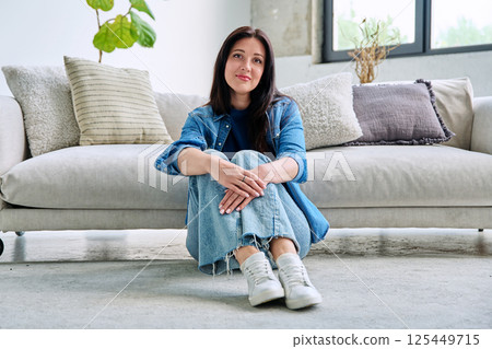 Portrait of beautiful young brunette woman sitting on sofa in living room Portrait of beautiful young brunette woman sitting on sofa in living room 125449715