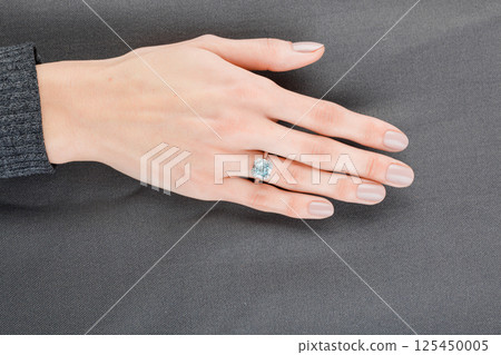 Beautiful female hand with gold ring with diamonds and aquamarine on gray background Beautiful female hand with gold ring with diamonds and aquamarine on gray background 125450005