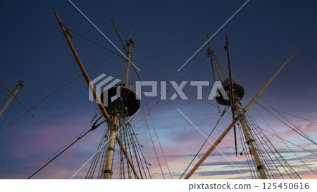 Old sailing ship masts reaching towards the twilight sky with vibrant colors illuminating the horizon Old sailing ship masts reaching towards the twilight sky with vibrant colors illuminating the horizon 125450616