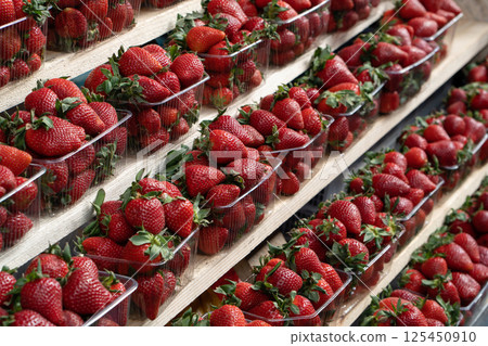Close-up of ripe strawberries for sale on market stall. Fresh strawberries in plastic cups displayed at a street market stall 125450910