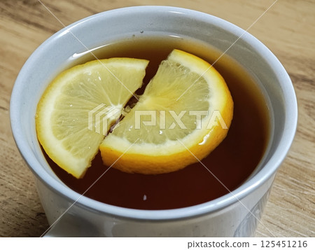 Two lemon slices floating in a cup of black tea on wooden table Two lemon slices floating in a cup of black tea on wooden table 125451216