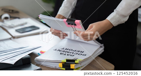 Detail-oriented professional sorting documents with binder clips and notes 125452016