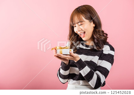 Portrait of happy beautiful Asian young woman smiling holding small gift box on hands, studio shot isolated on pink background, gift for you. Birthday, New year, Christmas, valentine day concept 125452028