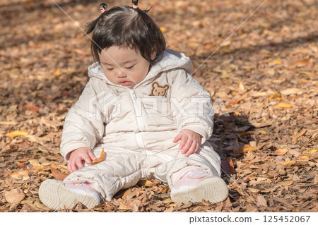 [一名 1 歲的孩子坐在覆蓋著落葉的冬季公園裡玩耍] 125452067