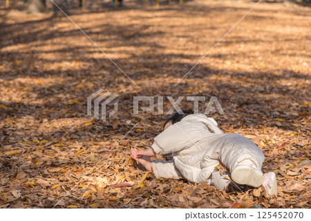 [一名一歲大的小孩躺在落葉覆蓋的冬季公園玩耍] 125452070