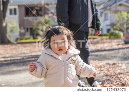 [One-year-old child standing and playing with his mother in a winter park covered with fallen leaves] 125452073