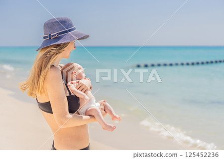 Mother holding her newborn baby by the turquoise sea, sharing a peaceful and loving moment. Family bonding, motherhood, and travel with baby concept Mother holding her newborn baby by the turquoise sea, sharing a peaceful and loving moment. Family bonding, motherhood, and travel with baby concept 125452236