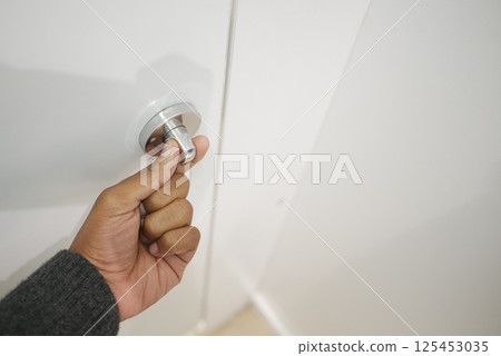 Hand turning a sleek silver door knob in a modern interior 125453035