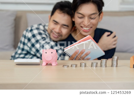 Diverse LGBTQ couple planning finances with piggy bank and coins at home. 125453269