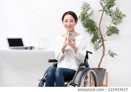 坐輪椅的女性透過家用智慧型手機工作 125453617