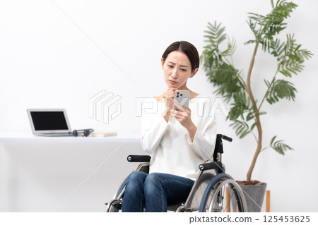 Woman in wheelchair working from home smartphone worries 125453625