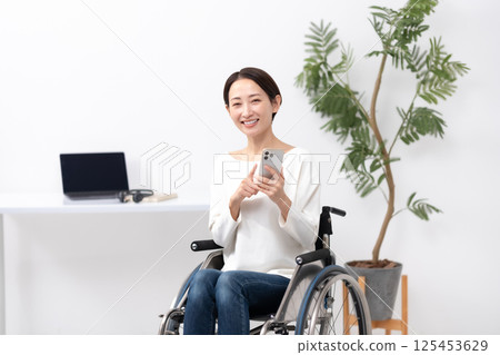 坐輪椅的女性透過家用智慧型手機工作 125453629