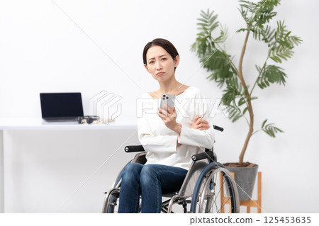 Woman in wheelchair working from home smartphone worries 125453635