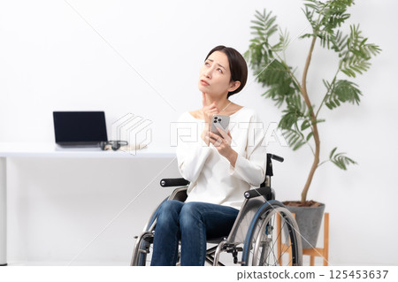 坐輪椅的女性在家使用智慧型手機工作時擔心 坐輪椅的女性在家使用智慧型手機工作時擔心 125453637
