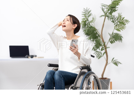Woman in wheelchair, working from home, worries 125453681