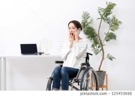 Woman in wheelchair, working from home, calling, surprised 125453698