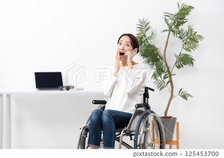 Woman in wheelchair, working from home, calling, surprised 125453700