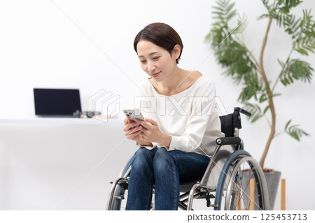 Woman in wheelchair, working from home, smartphone Woman in wheelchair, working from home, smartphone 125453713