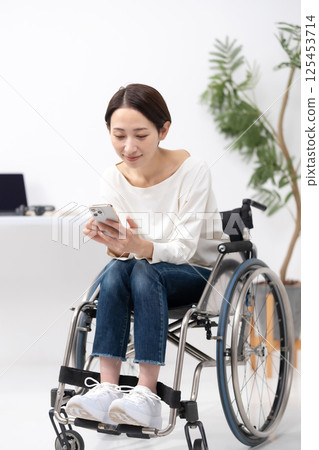 Woman in wheelchair, working from home, smartphone 125453714
