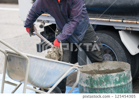 建築工地的混凝土工程（土木工程師將混凝土從半切的桶中轉移到手推車中） 125454305