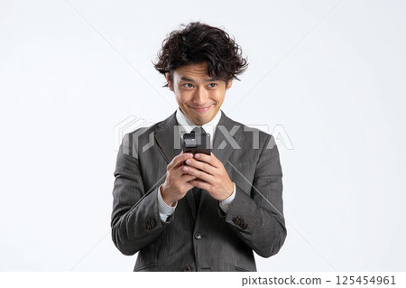 一位商人一邊看著他的智慧型手機一邊笑著 125454961