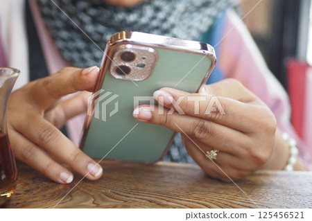 Woman using smartphone while sipping tea in cozy cafe setting 125456521