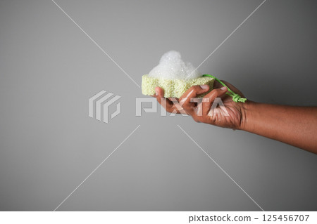 Hand holding a soapy cleaning sponge against a gray background Hand holding a soapy cleaning sponge against a gray background 125456707