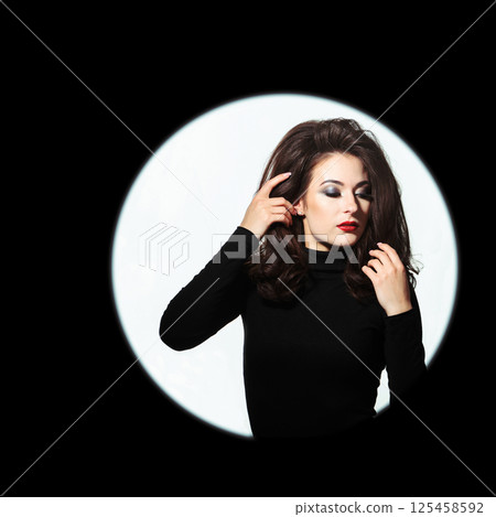 Beautiful woman standing in illuminated circle in black background Beautiful woman standing in illuminated circle in black background 125458592