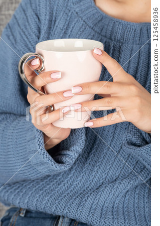 Woman with blue sweater holding cup of hot drink 125458936