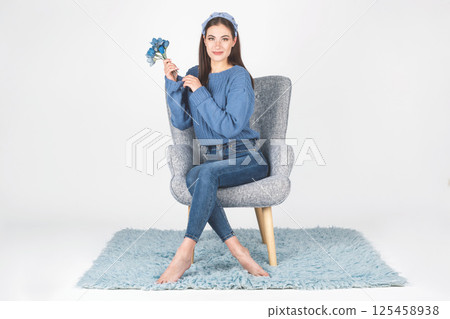 Woman with sweater, jeans and flowers sitting on armchair 125458938