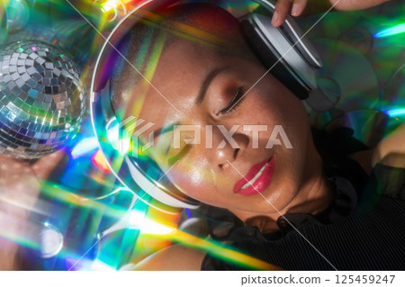 Happy Thai woman with headphones lying on glowing CD background Happy Thai woman with headphones lying on glowing CD background 125459247