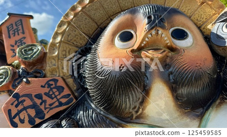 A close-up of a smiling Shigaraki ware raccoon dog and a lucky charm 125459585