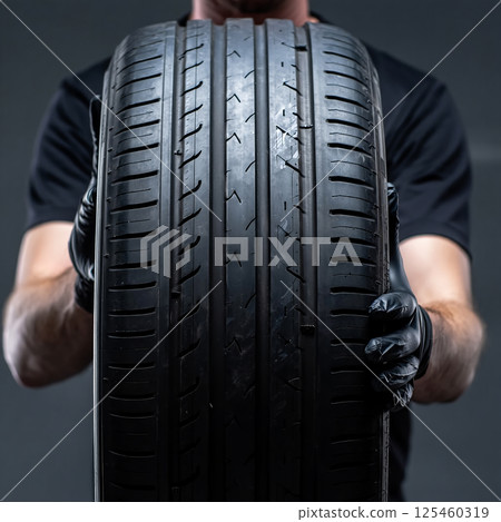 A pair of hands carefully hold a modern car tire, showing off the tread pattern. A pair of hands carefully hold a modern car tire, showing off the tread pattern. 125460319