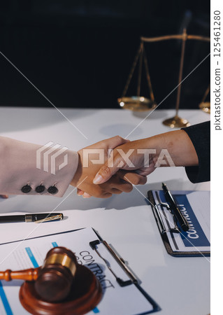 Two businesspeople are shaking hands in a law office with a scale and a gavel on the table Two businesspeople are shaking hands in a law office with a scale and a gavel on the table 125461280