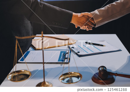 Two businesspeople are shaking hands in a law office with a scale and a gavel on the table Two businesspeople are shaking hands in a law office with a scale and a gavel on the table 125461288