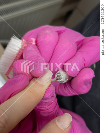 Close-up of electric nail drill manicure procedure by technician in pink gloves 125461309