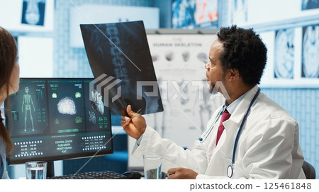 Medic expert showing the x ray imaging test results to patient at check up, discussing about treatment. Doctor pointing at radiography scans for interpretation, diagnostic report. Camera A. 125461848