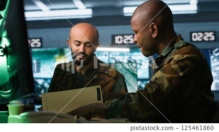 Teamworking military agents look at intel folder files on enemy battle formation. Intelligence corps coworkers read mission case documents to collect data on opponents strategy, camera A 125461860