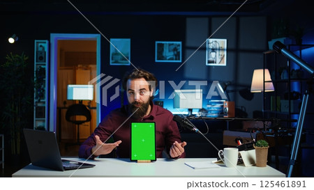 Tech specialist presenting chroma key tablet in entry level low budget price range to interested viewers, filming in studio. Viral content creator reviewing green screen digital device, camera B 125461891