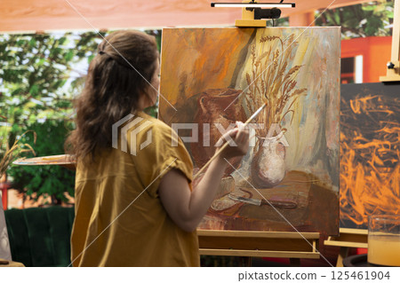 In a rustic workshop, artist mixes a variety of watercolor paint on a palette to create a colorful masterpiece on canvas. Woman painting with a brush and showing her skill, artwork creation. In a rustic workshop, artist mixes a variety of watercolor paint on a palette to create a colorful masterpiece on canvas. Woman painting with a brush and showing her skill, artwork creation. 125461904