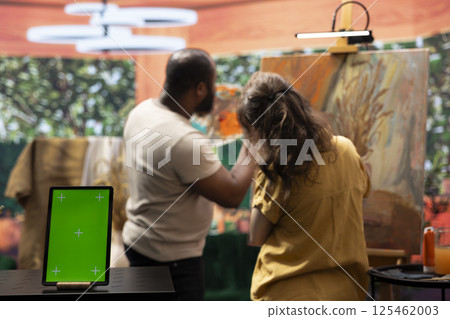 Skilled painters working on an artistic creation next to chroma key screen, using watercolor paint and brush kit to create a masterpiece. Two diverse artists enjoying their creative hobby. Skilled painters working on an artistic creation next to chroma key screen, using watercolor paint and brush kit to create a masterpiece. Two diverse artists enjoying their creative hobby. 125462003