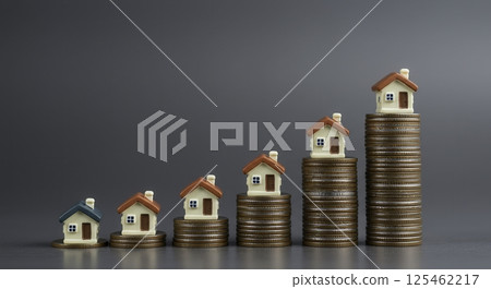 Stacks of coins increase in height with miniature houses on top, symbolizing rising real estate values and investment growth. Represents financial planning and property market trends. 125462217