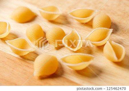 Raw uncooked dried Conchiglie shell pasta. Italian seashells pasta on wooden background. Raw uncooked dried Conchiglie shell pasta. Italian seashells pasta on wooden background. 125462470