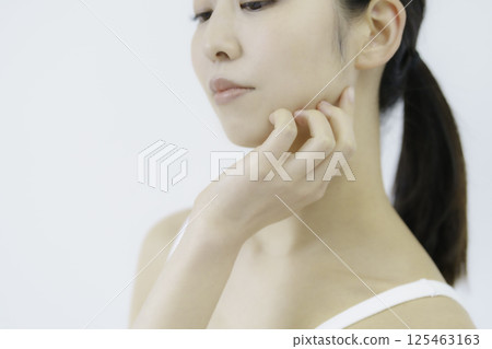 Close-up of a young woman's face with her hand on her cheek against a white background Close-up of a young woman's face with her hand on her cheek against a white background 125463163