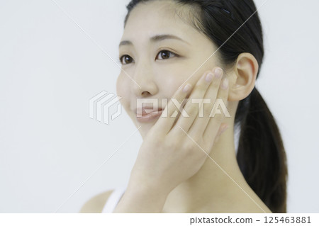 Close-up of a young woman's face touching her cheek against a white background 125463881
