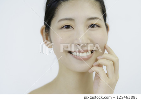 Close-up of a young woman's face touching her cheek against a white background Close-up of a young woman's face touching her cheek against a white background 125463883