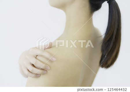 Close-up of a young woman's face holding her shoulders against a white background 125464432