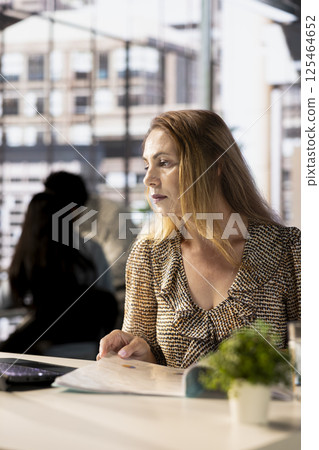 Corporate businesswoman reviewing data analytics at work, doing report writing to ensure project progress. Multinational company worker managing deadlines and financial planning. 125464652