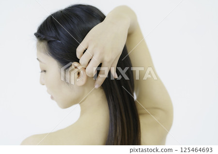 Close-up of a young woman's face turning around with her hand in her hair against a white background 125464693
