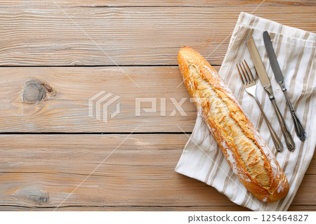 A golden crusted rustic French baguette rests on a wooden table with vintage cutlery A golden crusted rustic French baguette rests on a wooden table with vintage cutlery 125464827